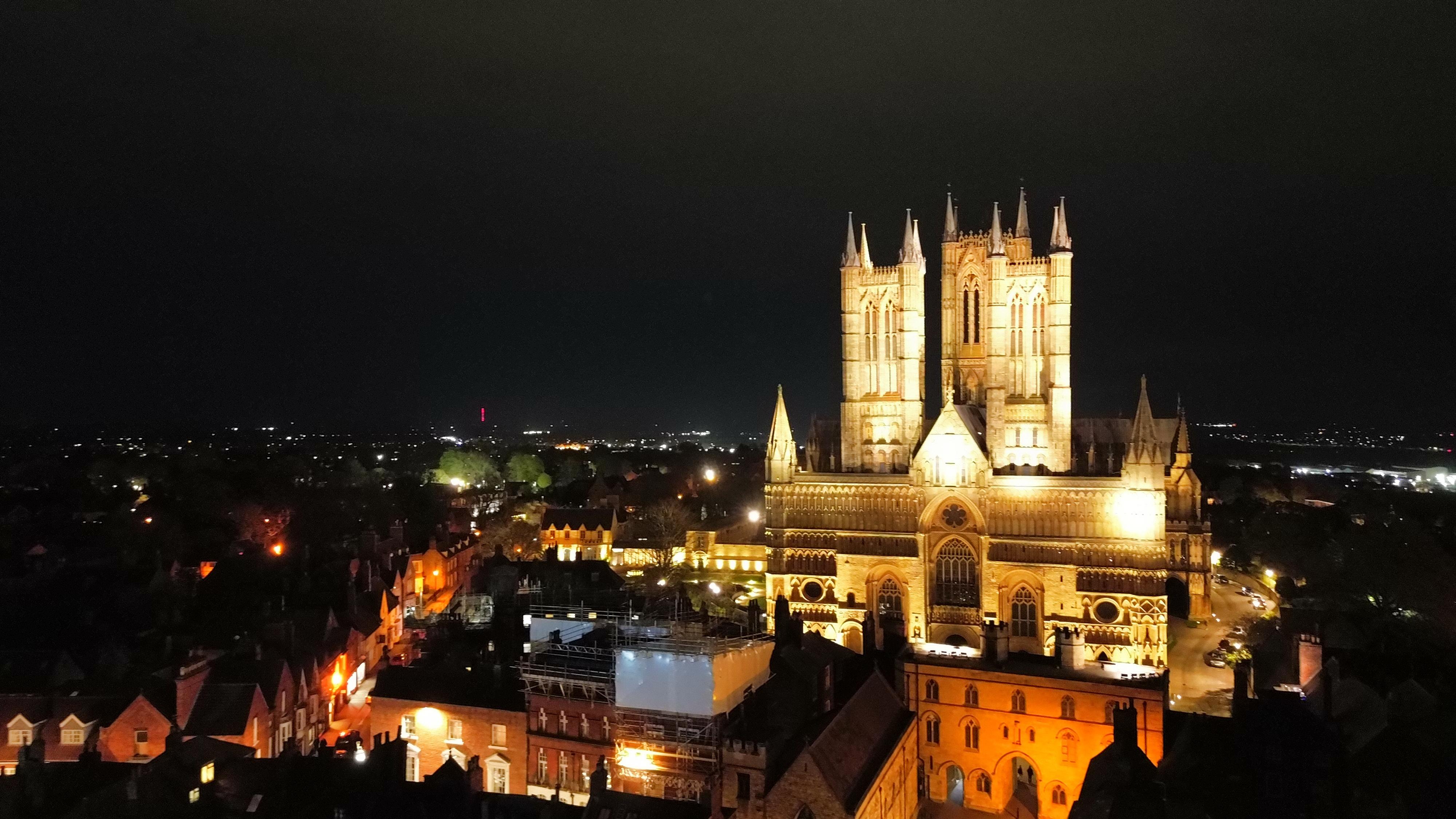 Night time photo of Lincoln Cathedral which is lit up in the foreground and the rest of the city is in the background in the dark.