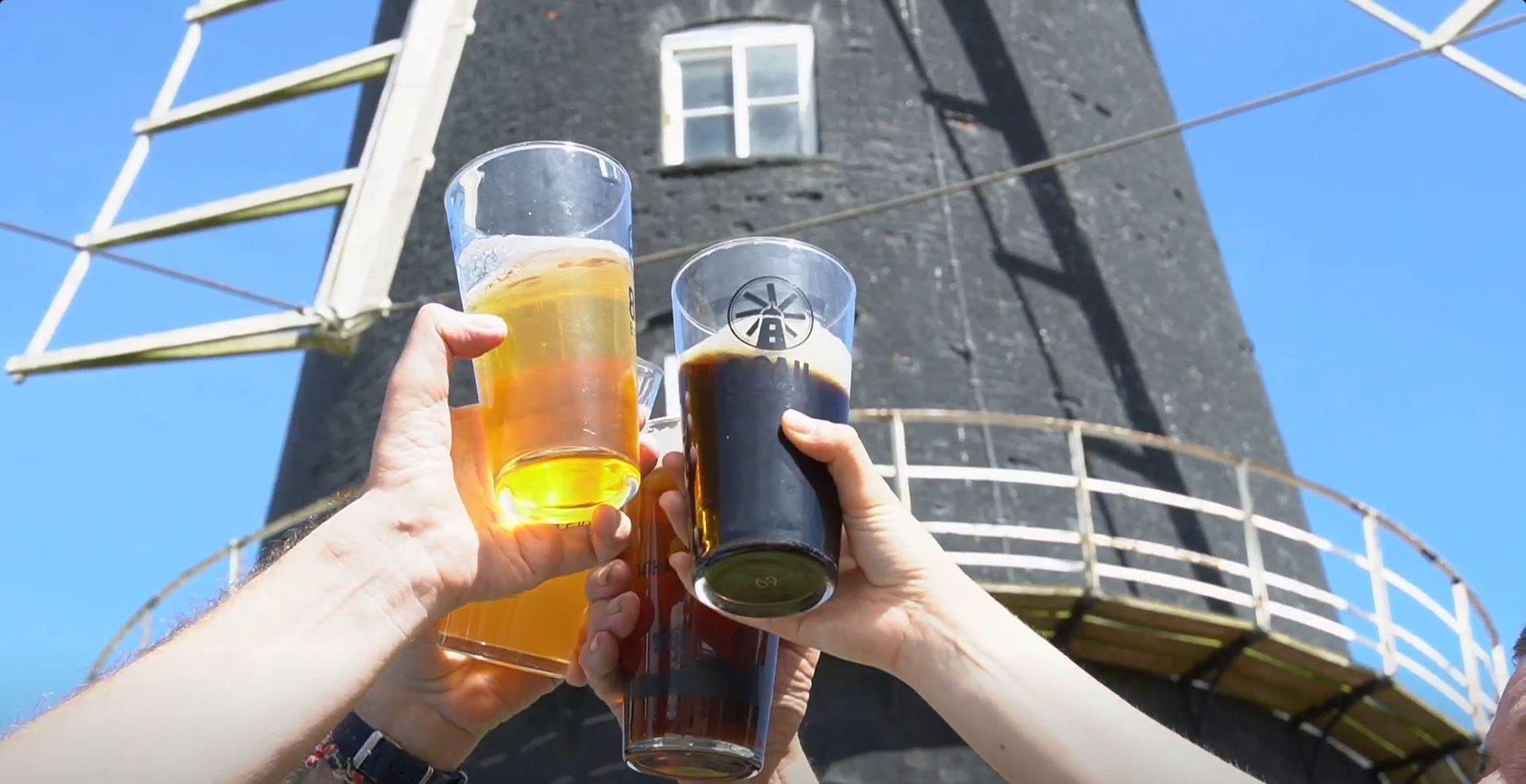 An image of four different beers being 'cheered' in the air in front of a windmill.