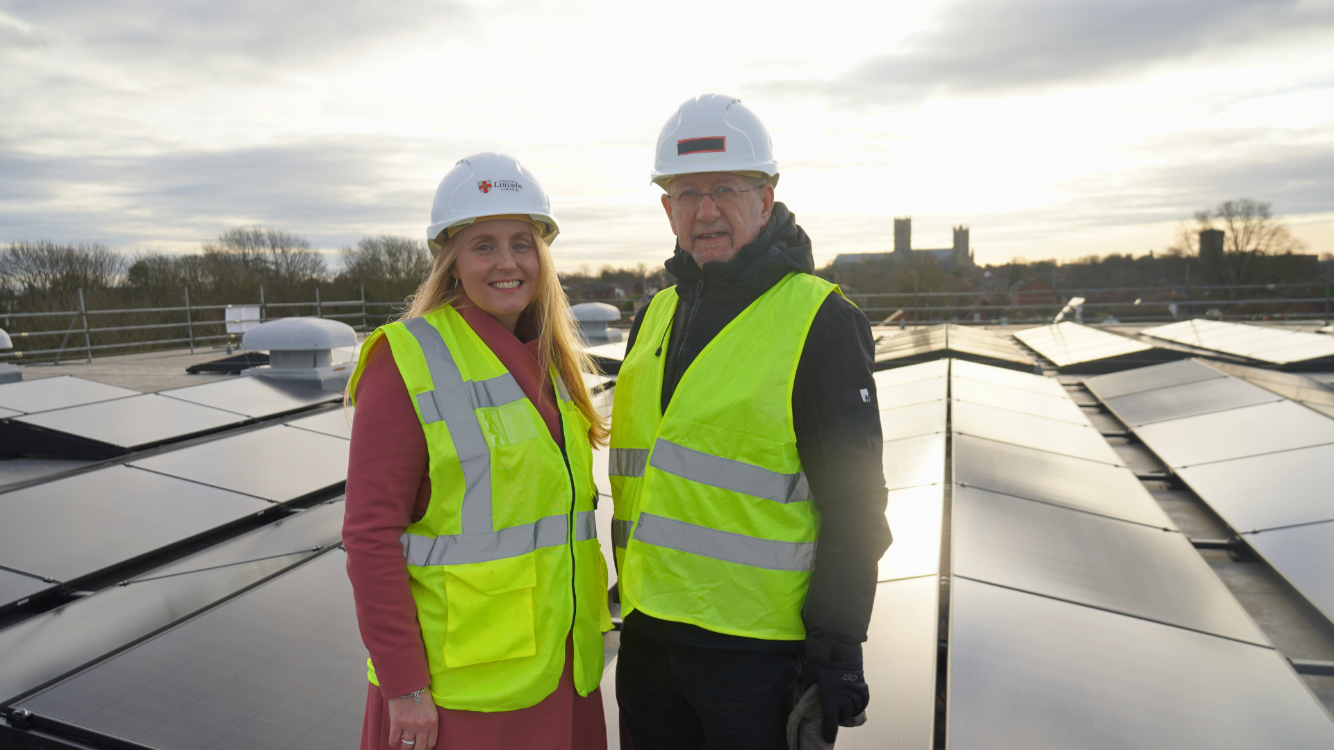 A woman and a man stood on a flat roof with solar panels behind them.