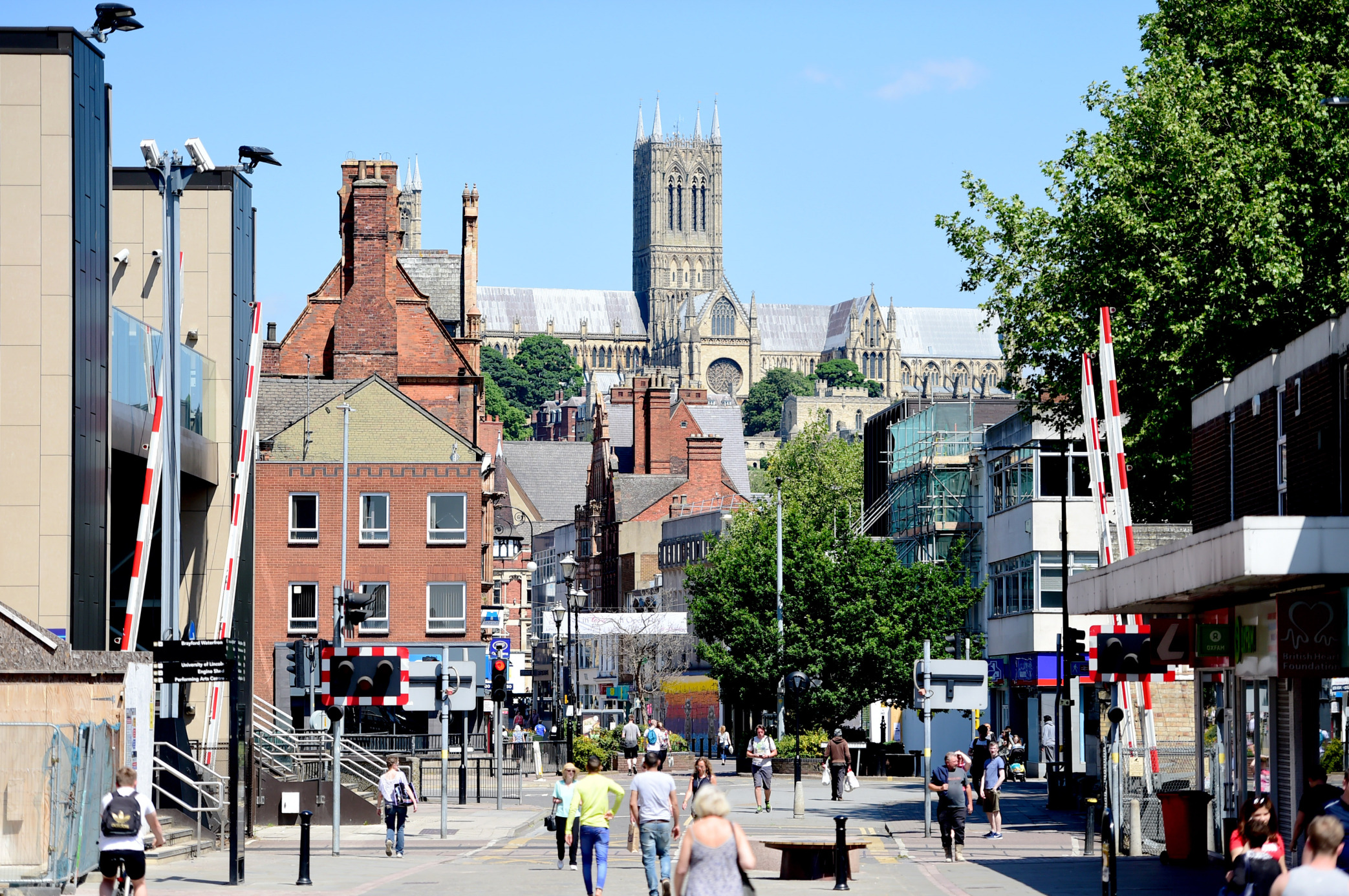 Lincoln Cathedral from the high street &ndash; city centre can be seen with lots of people walking through the centre of town, and a railway crossing.